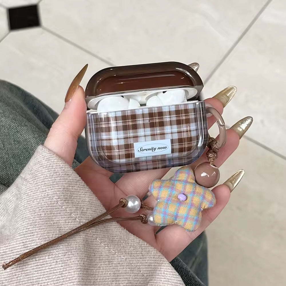 Plaid patterned airpod case held by a hand with decorative nails on a neutral background