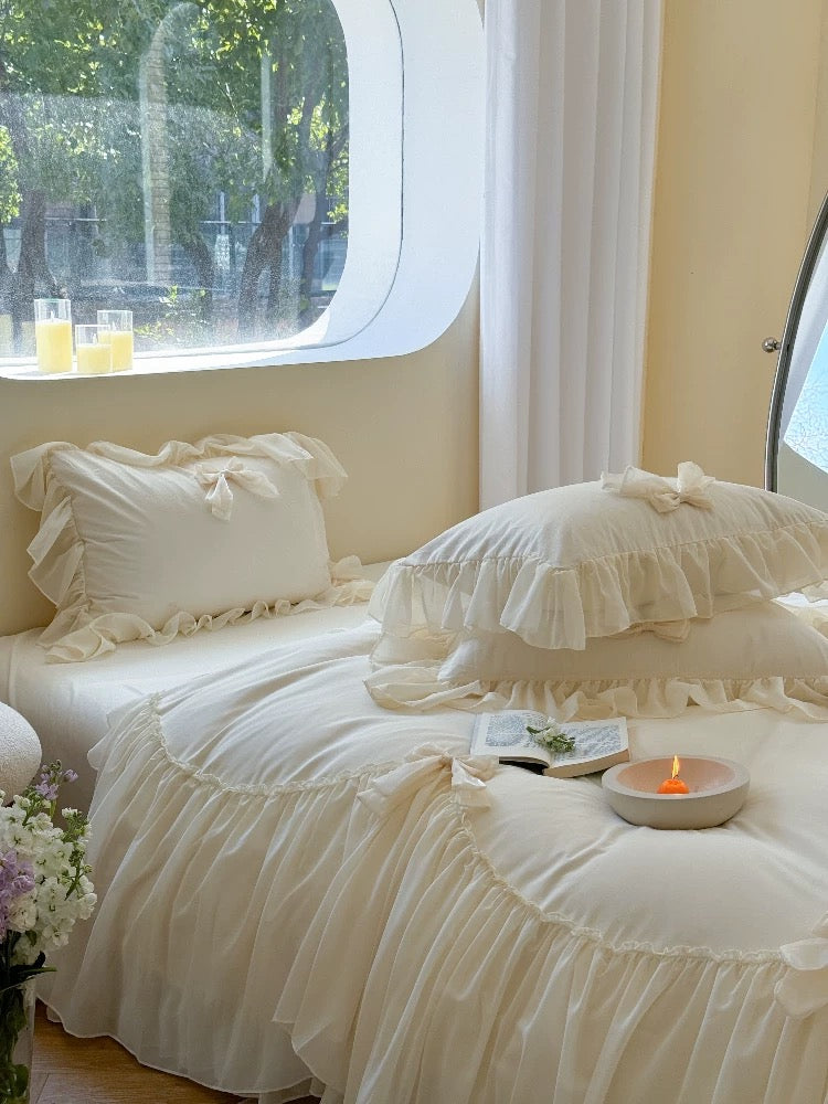 Delicate white bedding with ruffled pillows in a softly lit room.