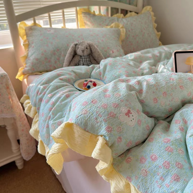 Sage green floral duvet cover with yellow crinkled ruffle trim styled on a white bed frame
