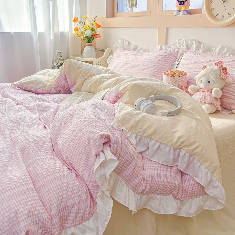 Pink and white checkered bedding with a teddy bear and headphones on a bed.