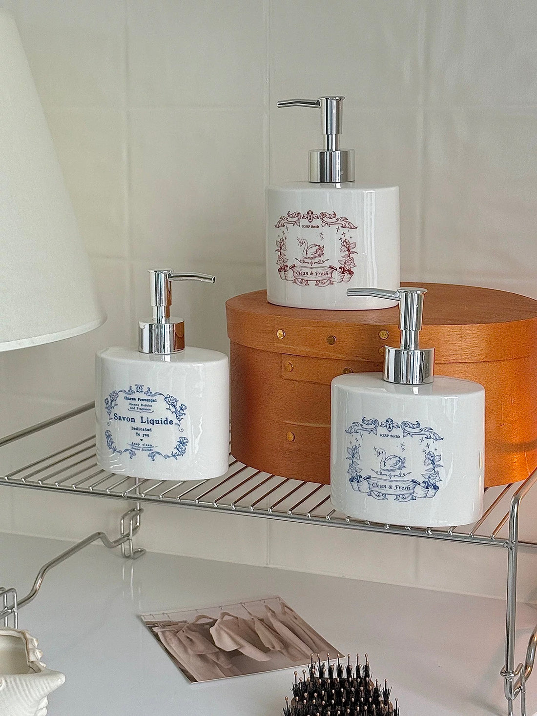 A Cottagecore soap dispenser display shows blue floral lettering and blue and red swan designs on a shelf.