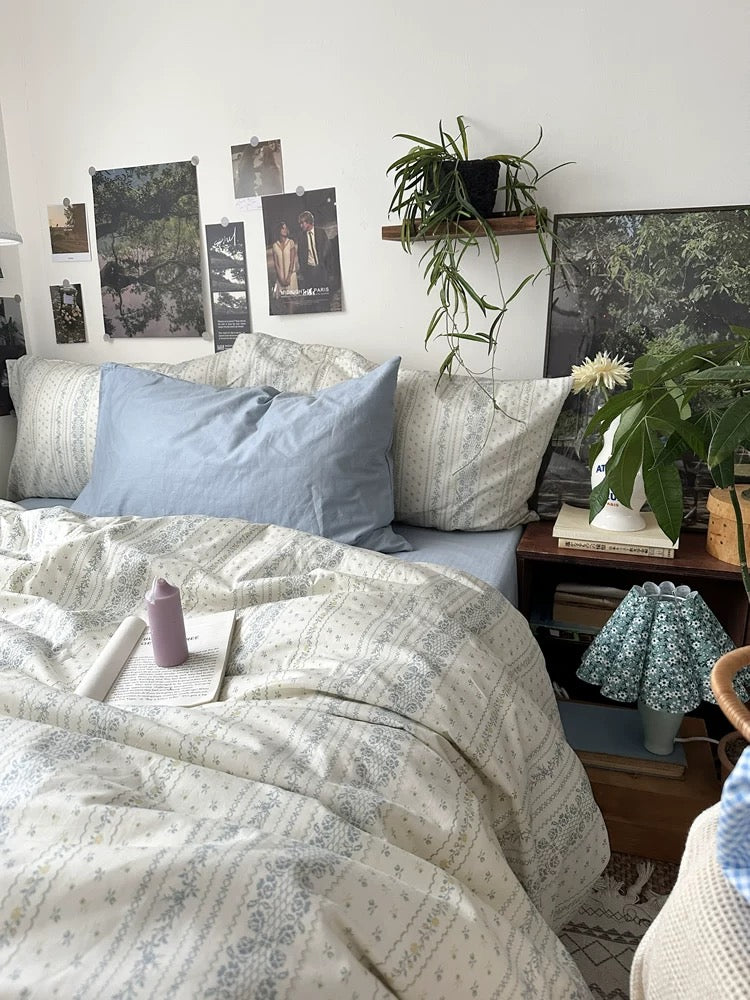 Breathable cotton bedding featuring delicate blue floral stripes styled inside bright European inspired bedroom with plants everywhere.