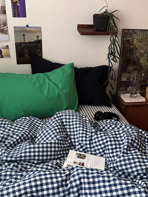 Bed with checkered duvet, green pillow, and black pillows against a wall with framed pictures.