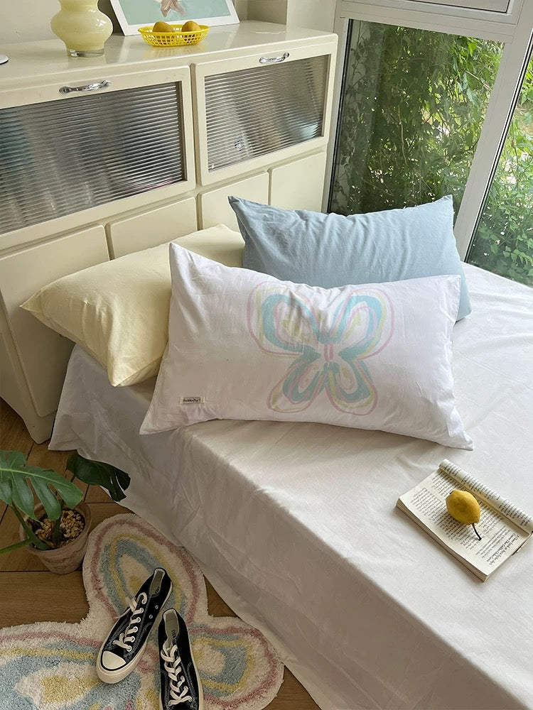 White cotton butterfly pillowcase styled with pastel bedding near a window.