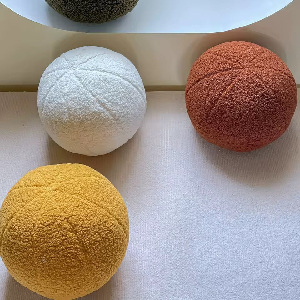 Four textured balls in white, orange, yellow, and green on a light surface.