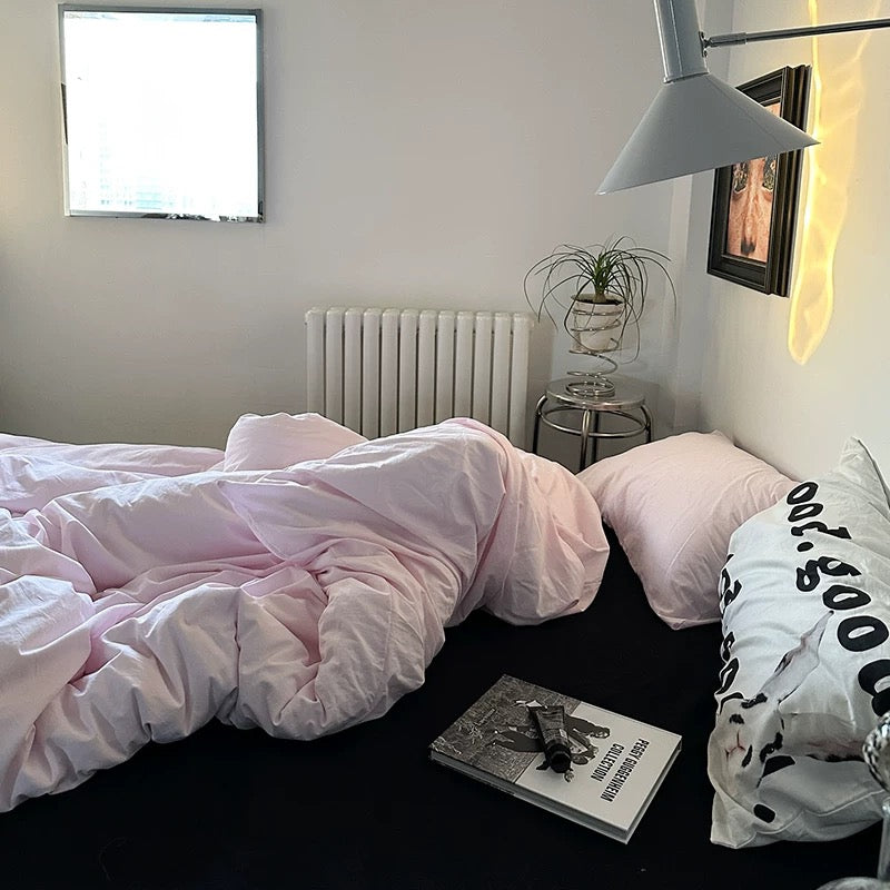 Bedroom with pink bedding, a book, and a lamp.