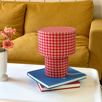 Red and white checkered lamp on a stack of books with a yellow sofa in the background