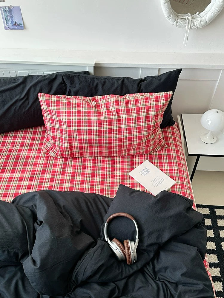 Red plaid blanket on a bed with black headphones and a book underneath, in a room setting.