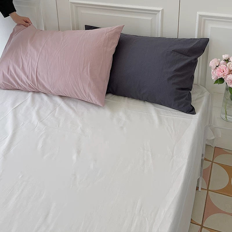 A cream-white sheet is styled with a pink pillow and a dark gray pillow against a paneled wall.