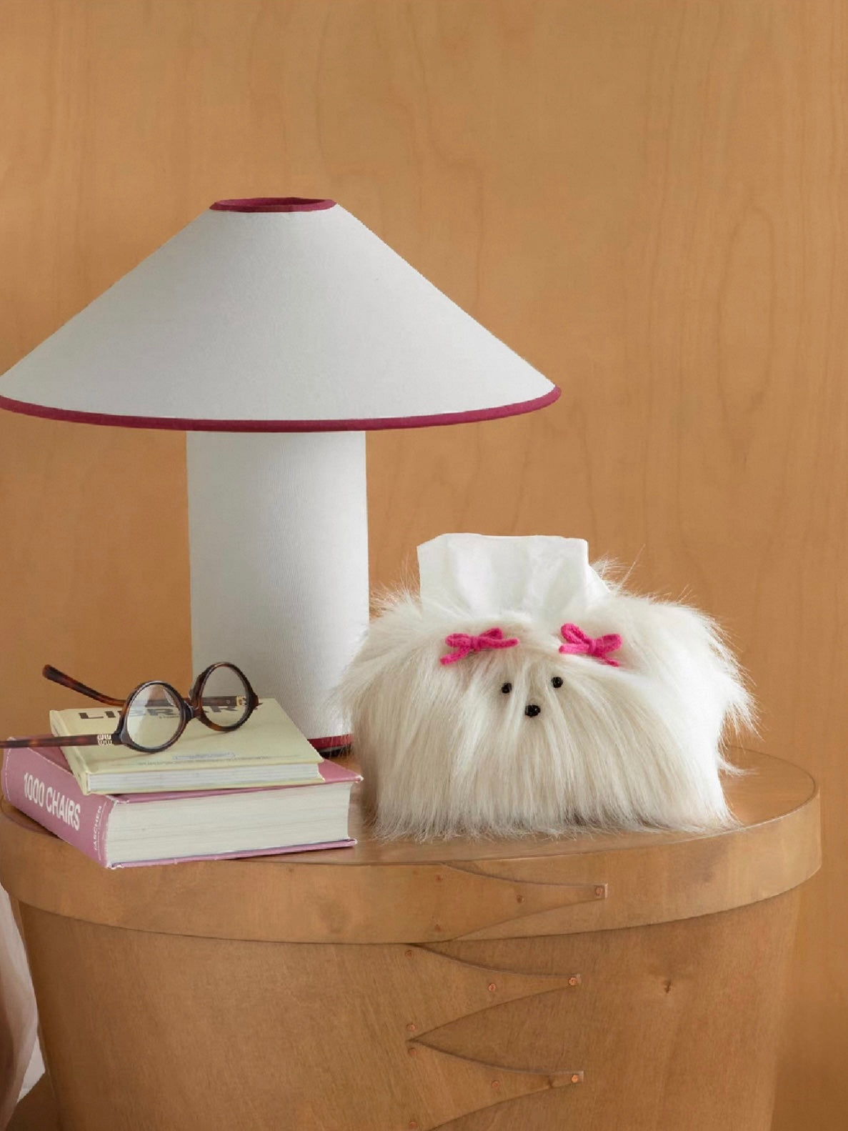 Cream White dog face tissue cover with pink bows stands on a wooden side table beside a white lamp.