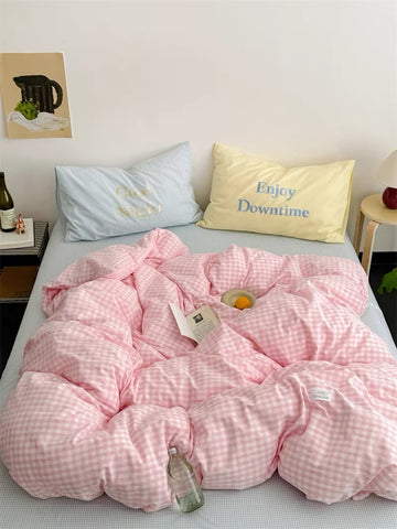 Pink checkered comforter on a bed with pillows and a bottle of wine.