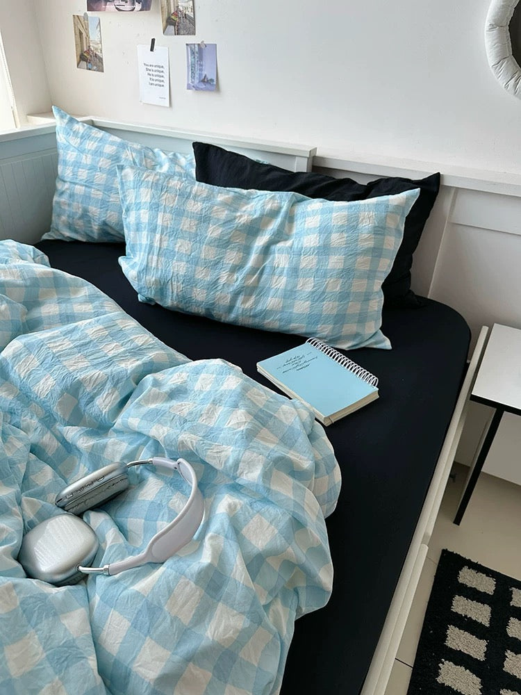 Bed with blue checkered bedding, pillows, and a notebook on a black bed frame.