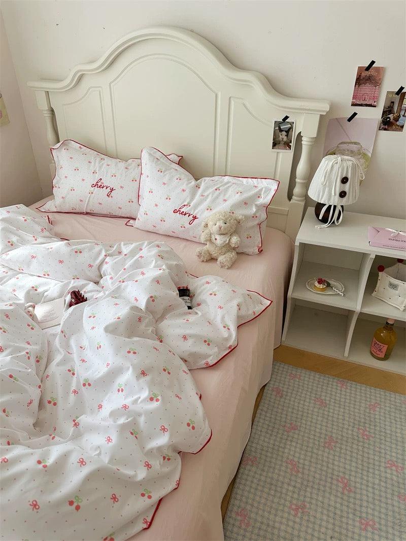 Bedroom with a bed featuring white bedding and pink accents, a nightstand with a lamp, and decorative items.