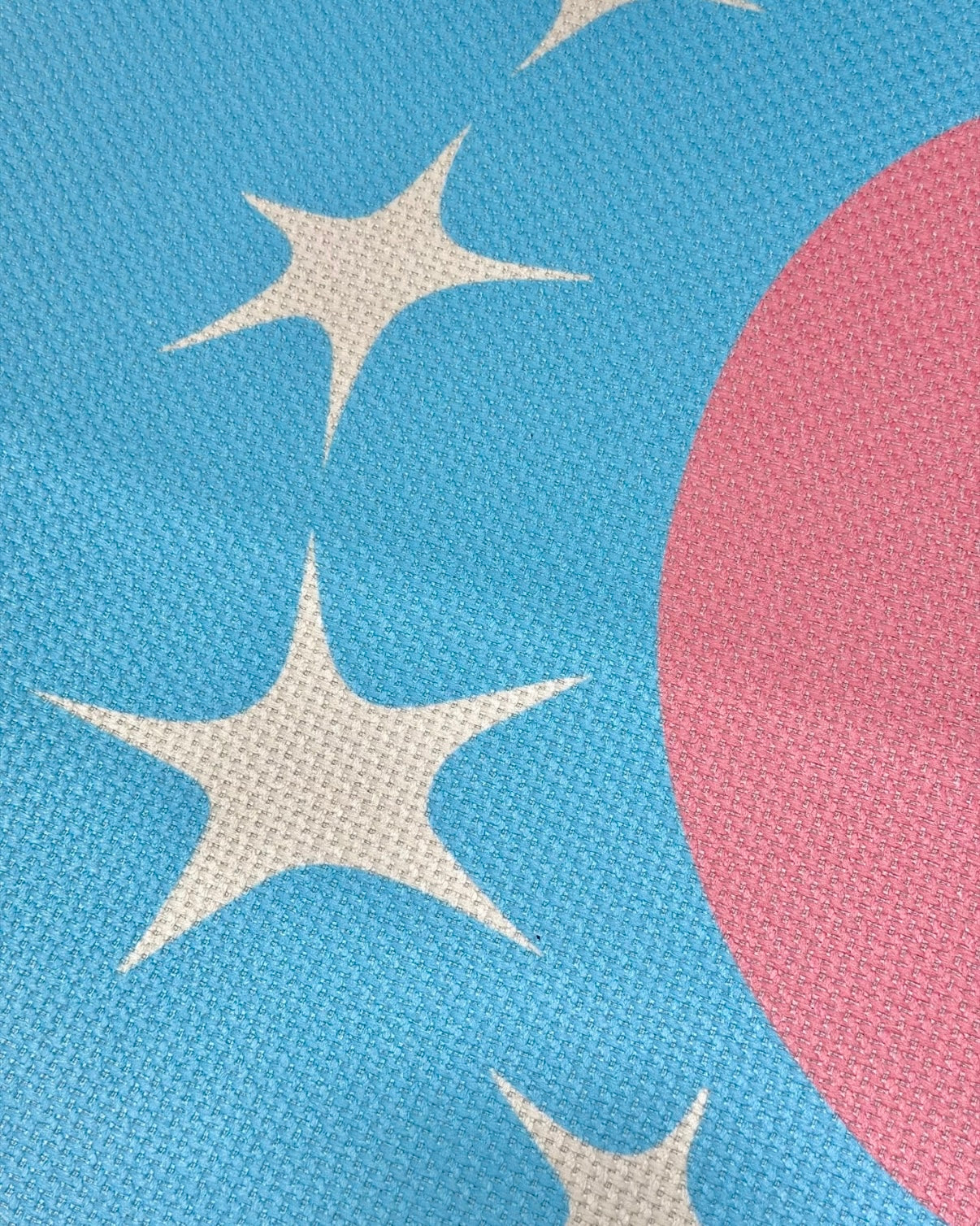 Close-up of a woven textile pattern featuring a bright blue background with cream star shapes and a large pink circular shape.