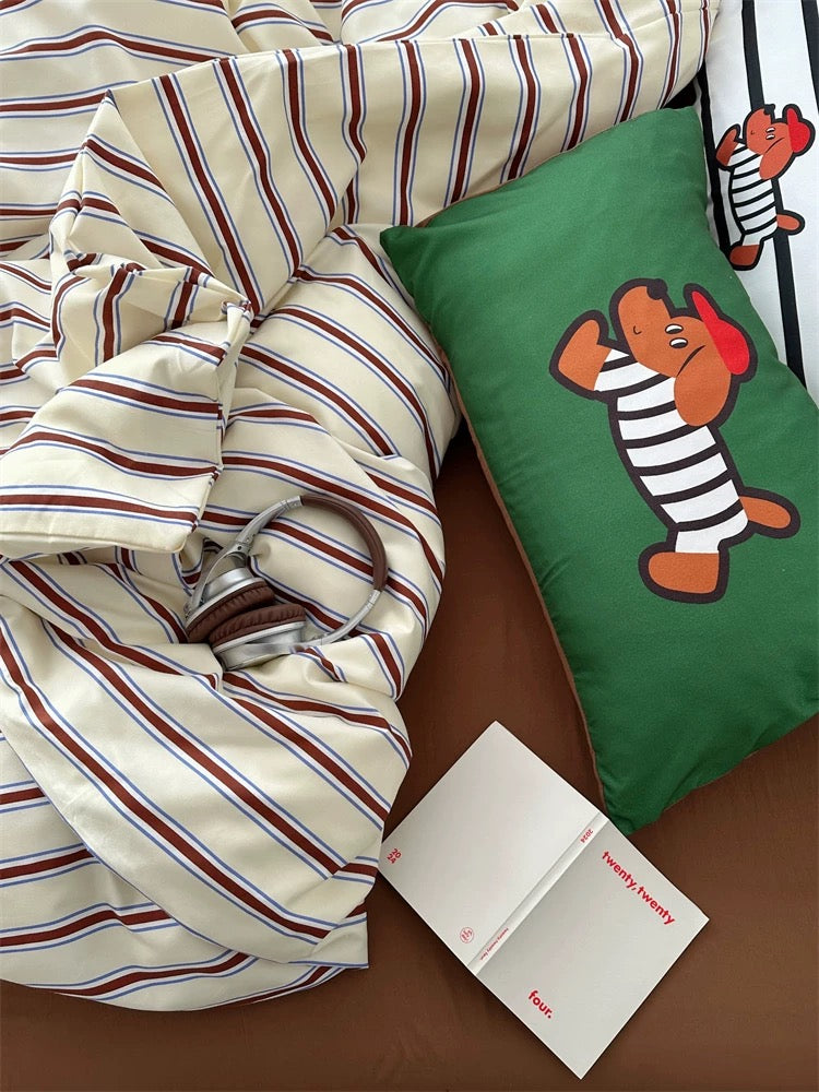 Striped duvet, green pillow with cartoon character, and white card on a brown surface