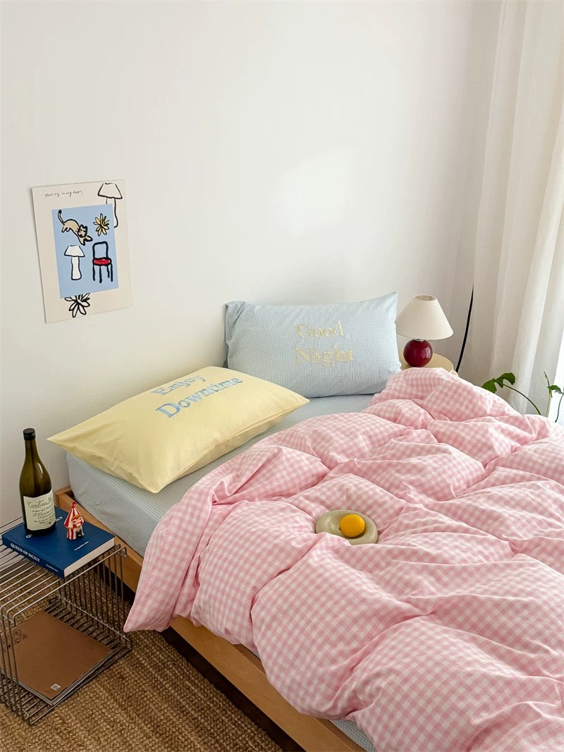 Bedroom with pink checkered duvet, yellow pillow, and blue pillow
