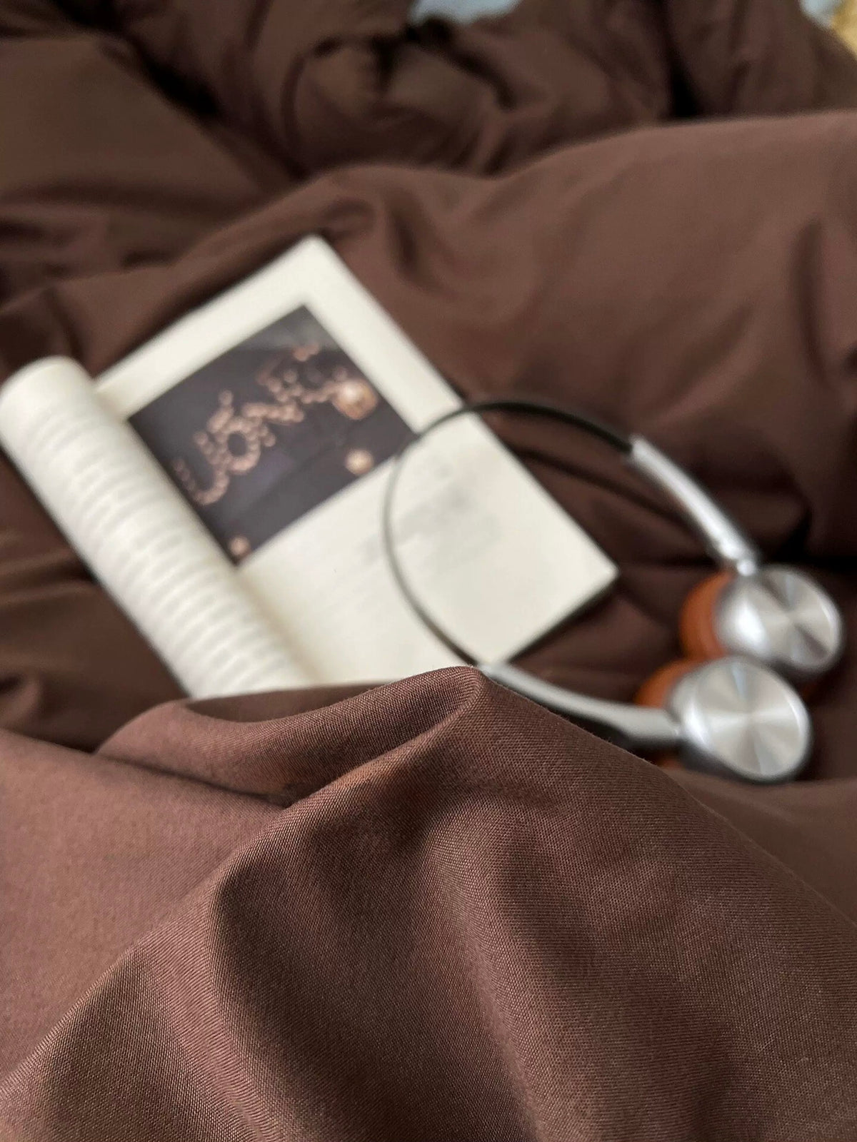 Dark brown bedding close-up with a book and headphones on the duvet cover