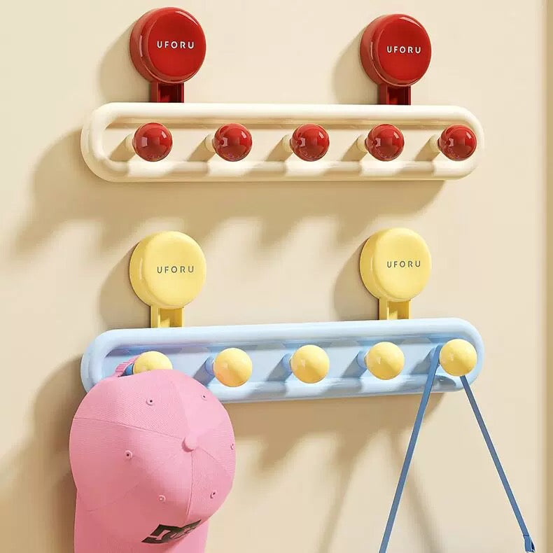 Colorful decorative wall hooks mounted on beige wall with pink cap and blue handbag hanging.