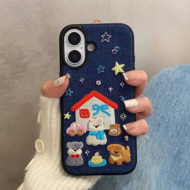 Phone case with embroidered design of a house, cat, dog, and teddy bear held by a person.