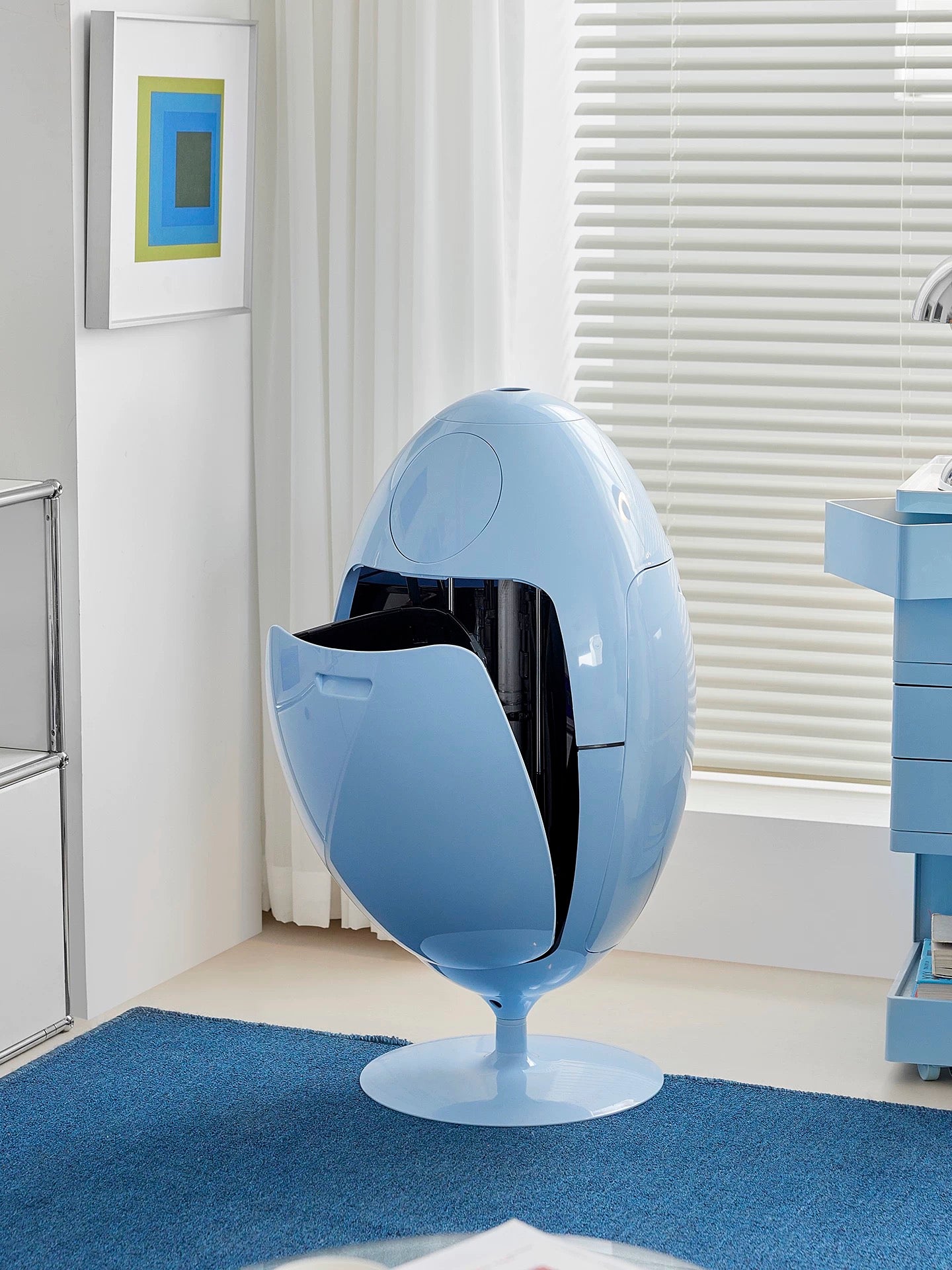 Blue egg-shaped chair in a room with a window and artwork on the wall.