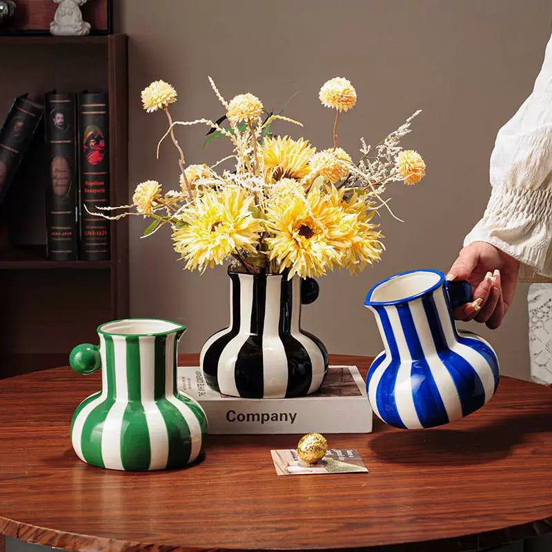 Three decorative vases with striped patterns on a wooden table, one of which is being held by a person.