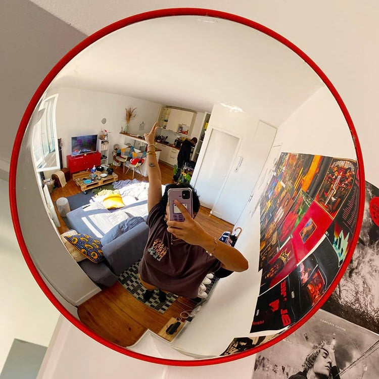 Person taking a mirror selfie in a room with a round mirror reflecting a living room.