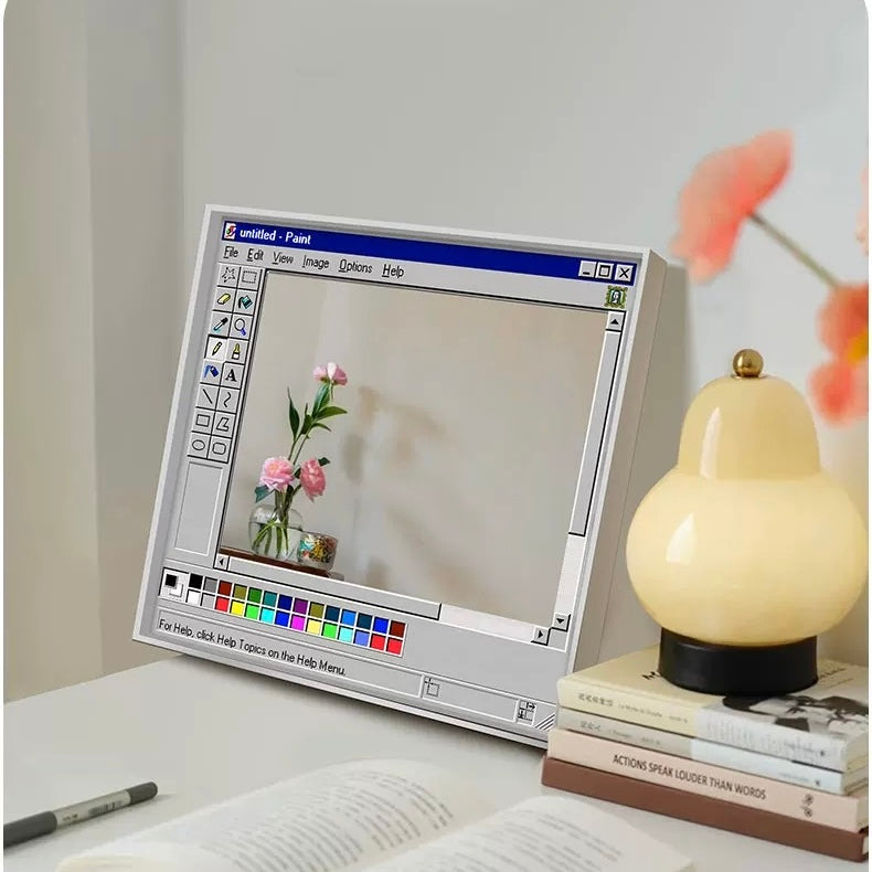 Vintage computer monitor displaying a flower image on a desk with books and a lamp.