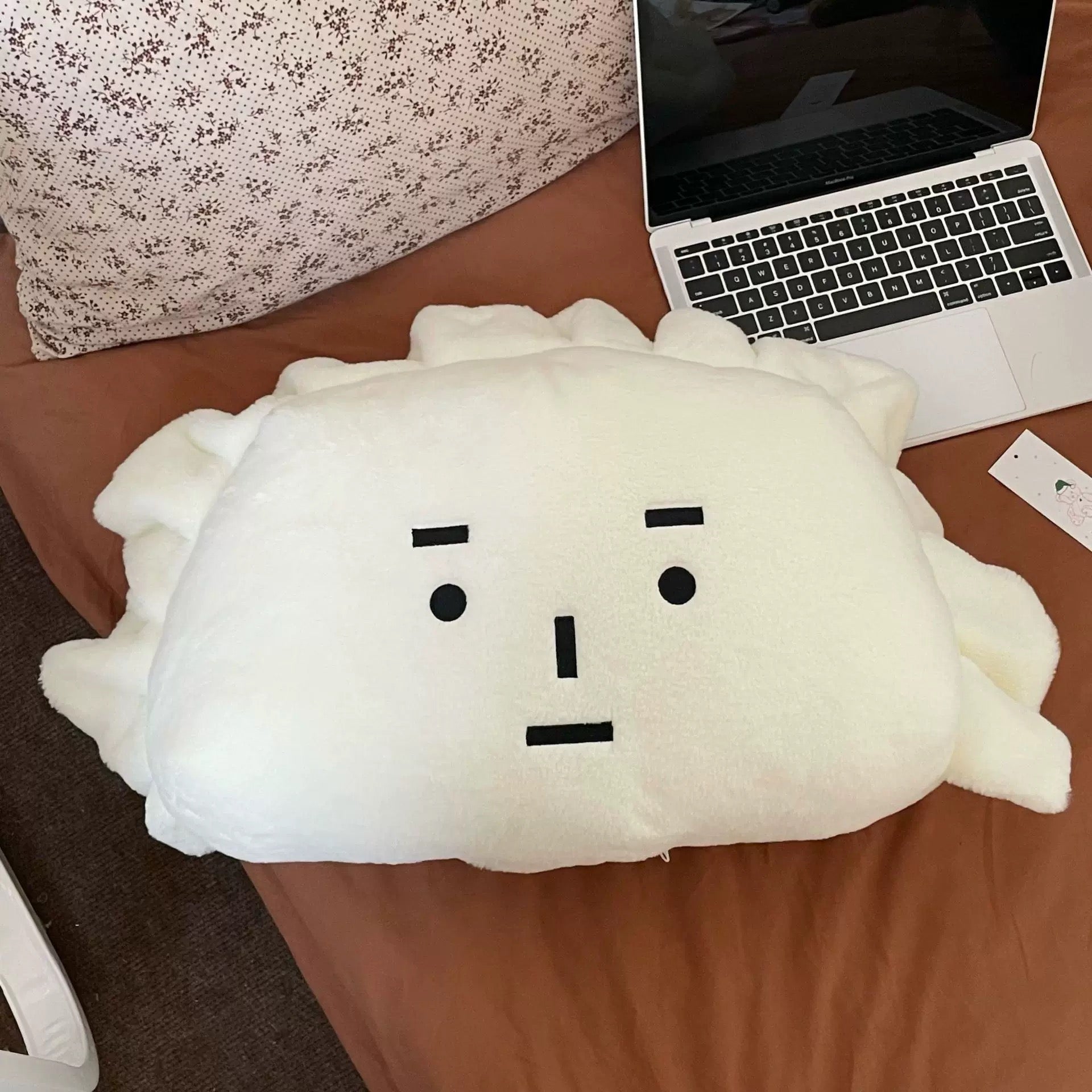Plush toy resembling a cloud with a face on a desk next to a laptop