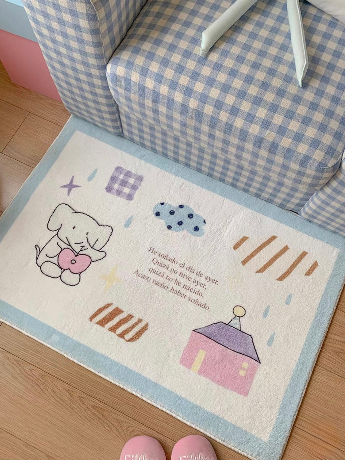 A blue bordered elephant rug shows an elephant holding a pink heart beside a house, stars and small patterned shapes.