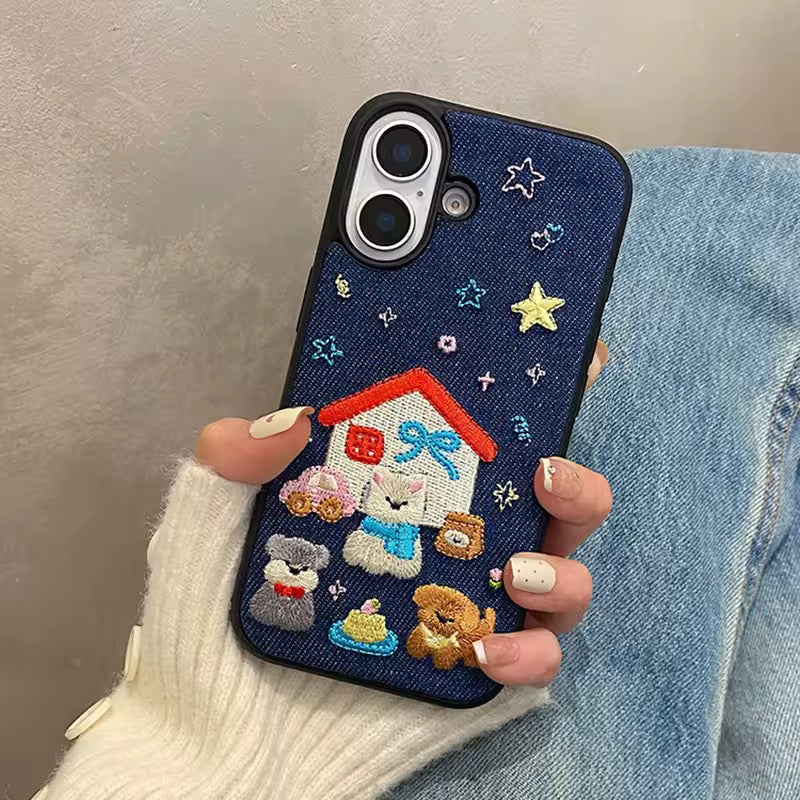 Phone case with embroidered design of a house, cat, dog, and teddy bear held by a person.