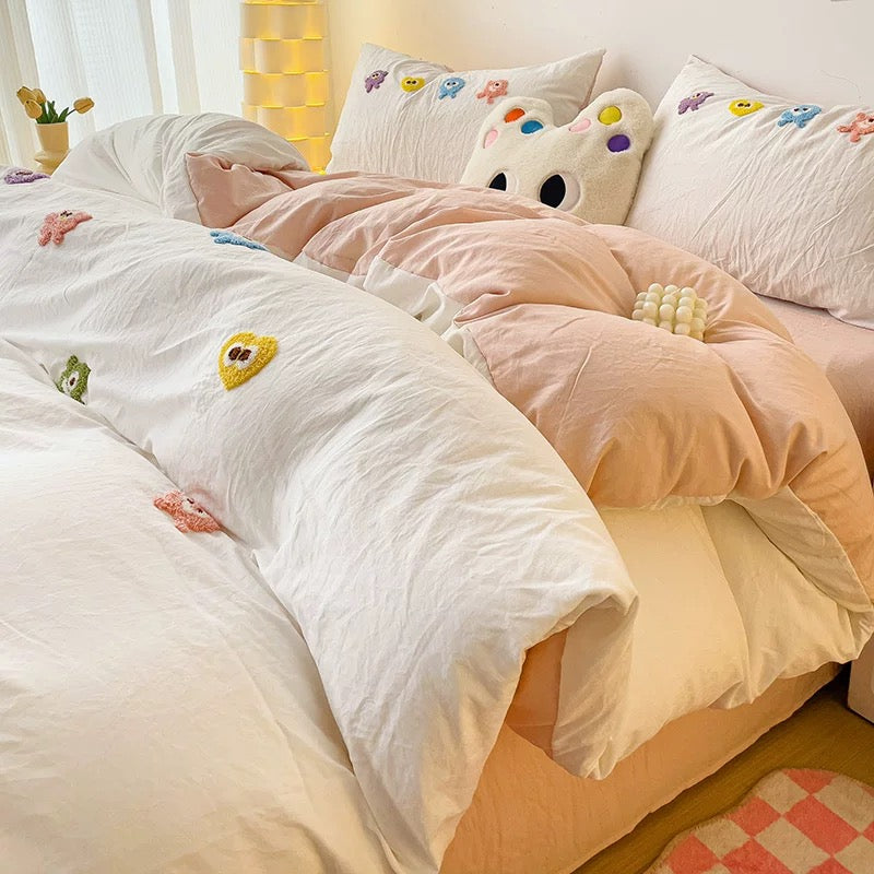 Side view of white embroidered duvet folded over pale pink bedding with matching cartoon pillowcases.