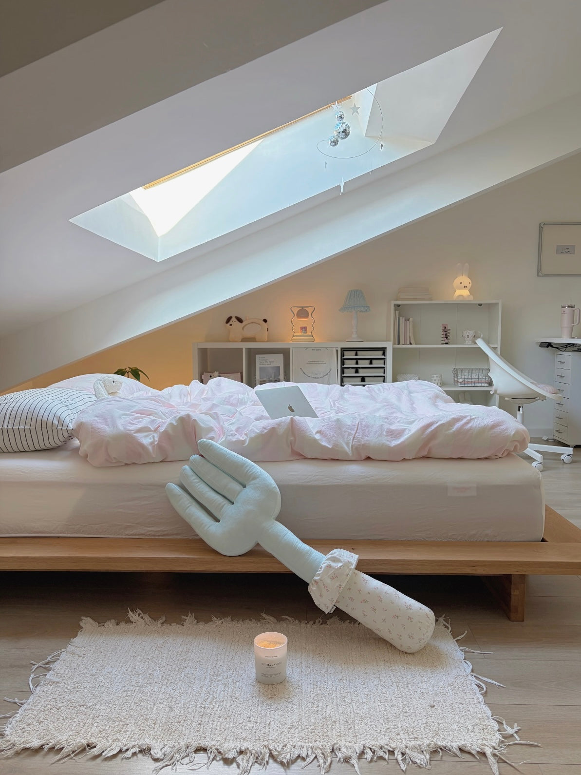A blue fork plush pillow leans diagonally in a wide bedroom view, with its pale handle pointing down.