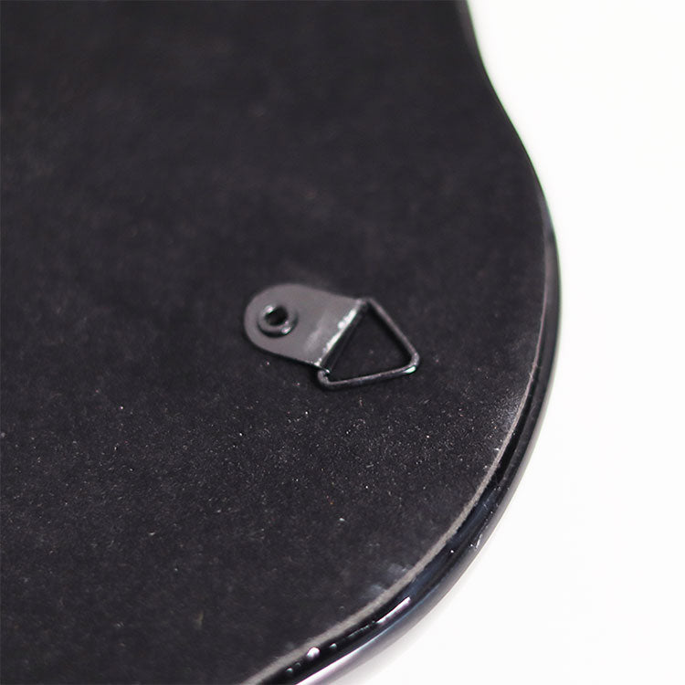 Close-up of the back corner of a black oval object, showing a small metal hanging loop attached to a textured black surface against a white background.