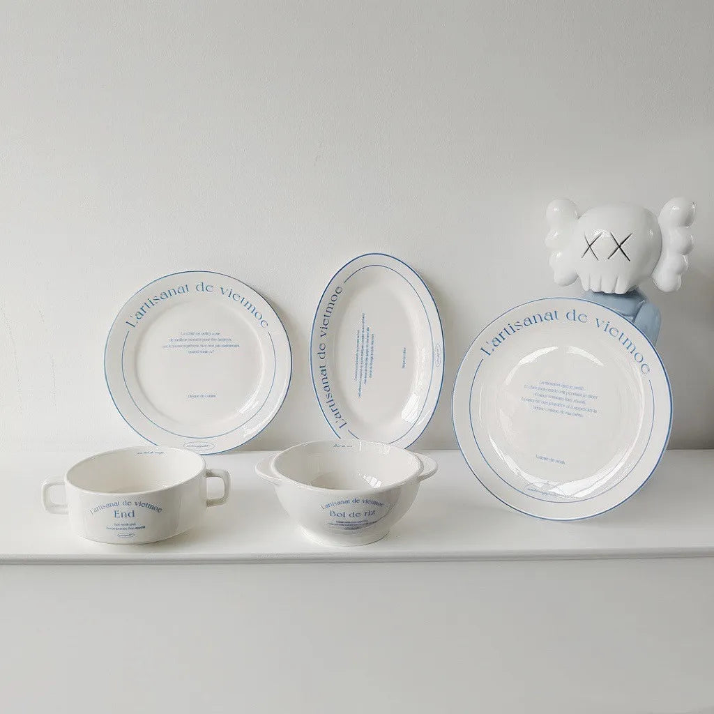 White French bistro ceramic plates and bowls with blue lettering arranged together on a table surface