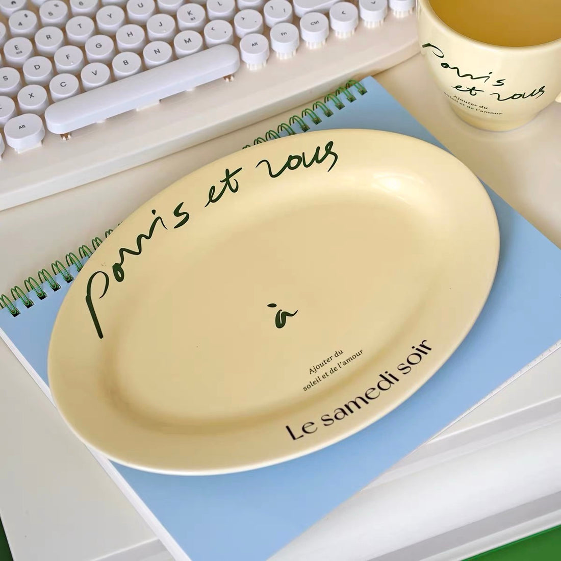 Cream porcelain mug and round plate with black French script displayed together on wooden tabletop
