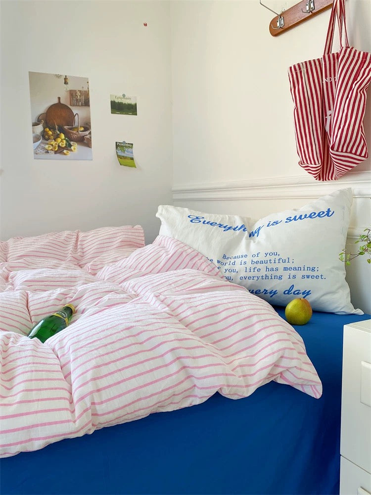 Bed with pink and white striped bedding and pillows, with a red and white bag hanging above.