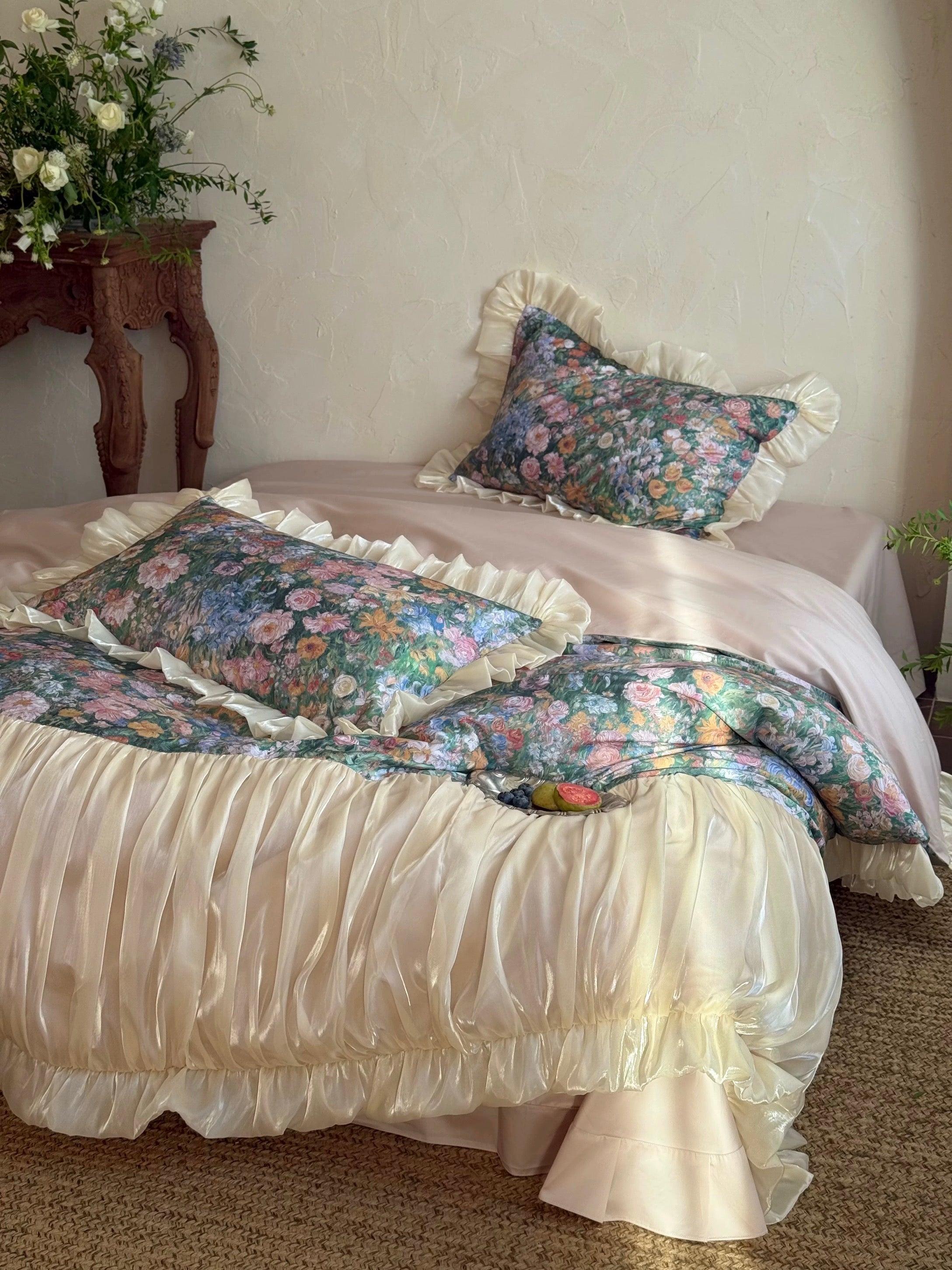 Floral bedding set on a bed with a decorative pillow and a vase of flowers on a table.