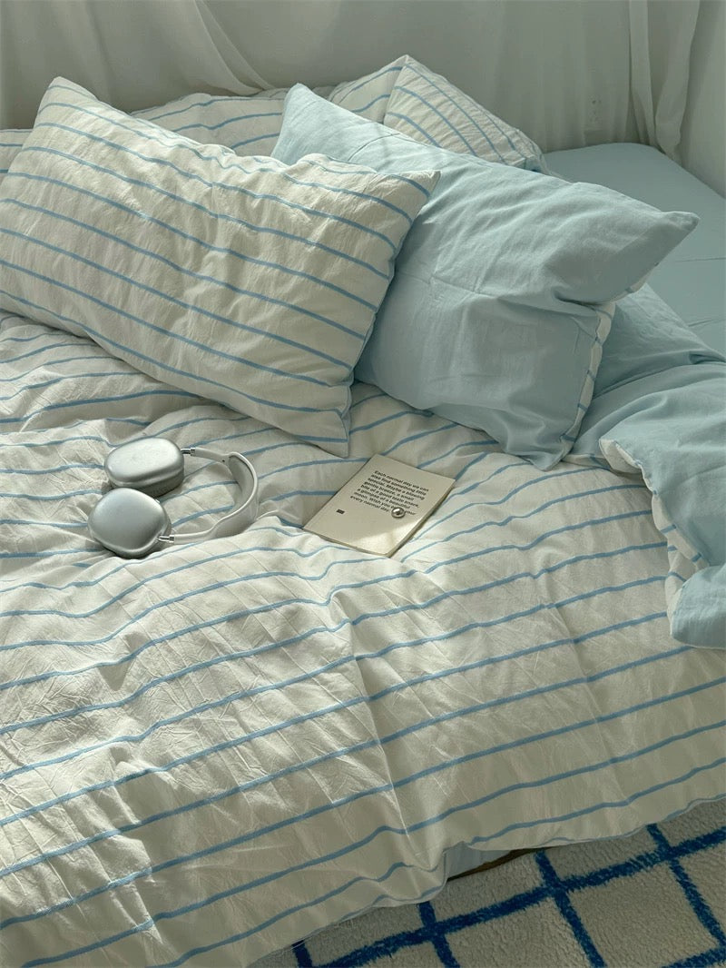 Light blue and white striped bedding on a bed with a book and small round objects.