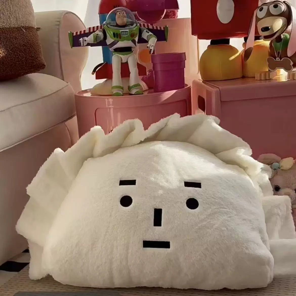 White plush toy with black facial features on a surface, with colorful toys in the background.