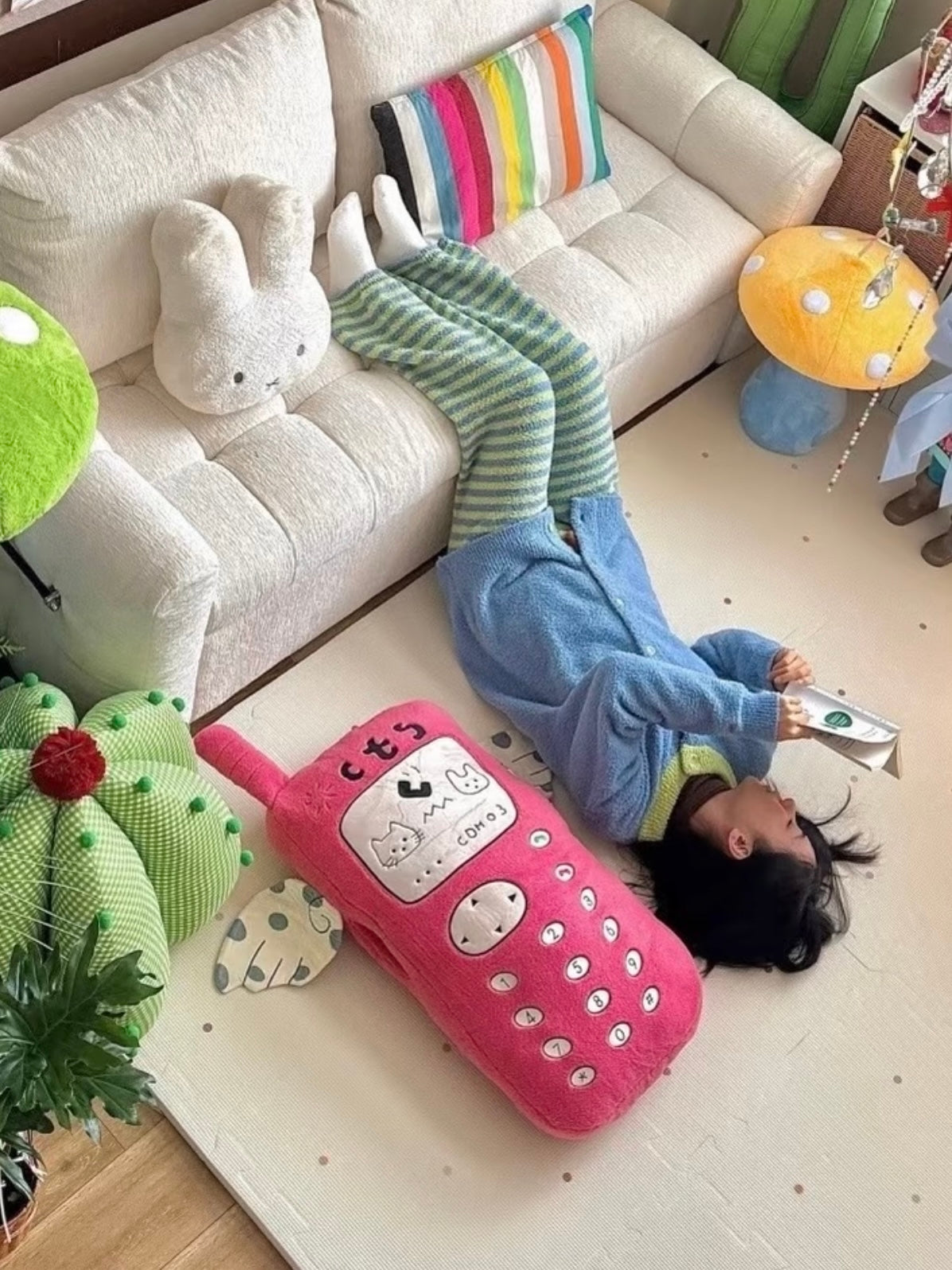 A pink giant phone pillow lies beside a person on the floor, with its embroidered keypad facing upward.