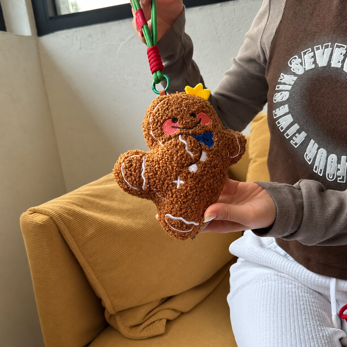 Mini gingerbread man plush keychain with hanging cord displayed by hand