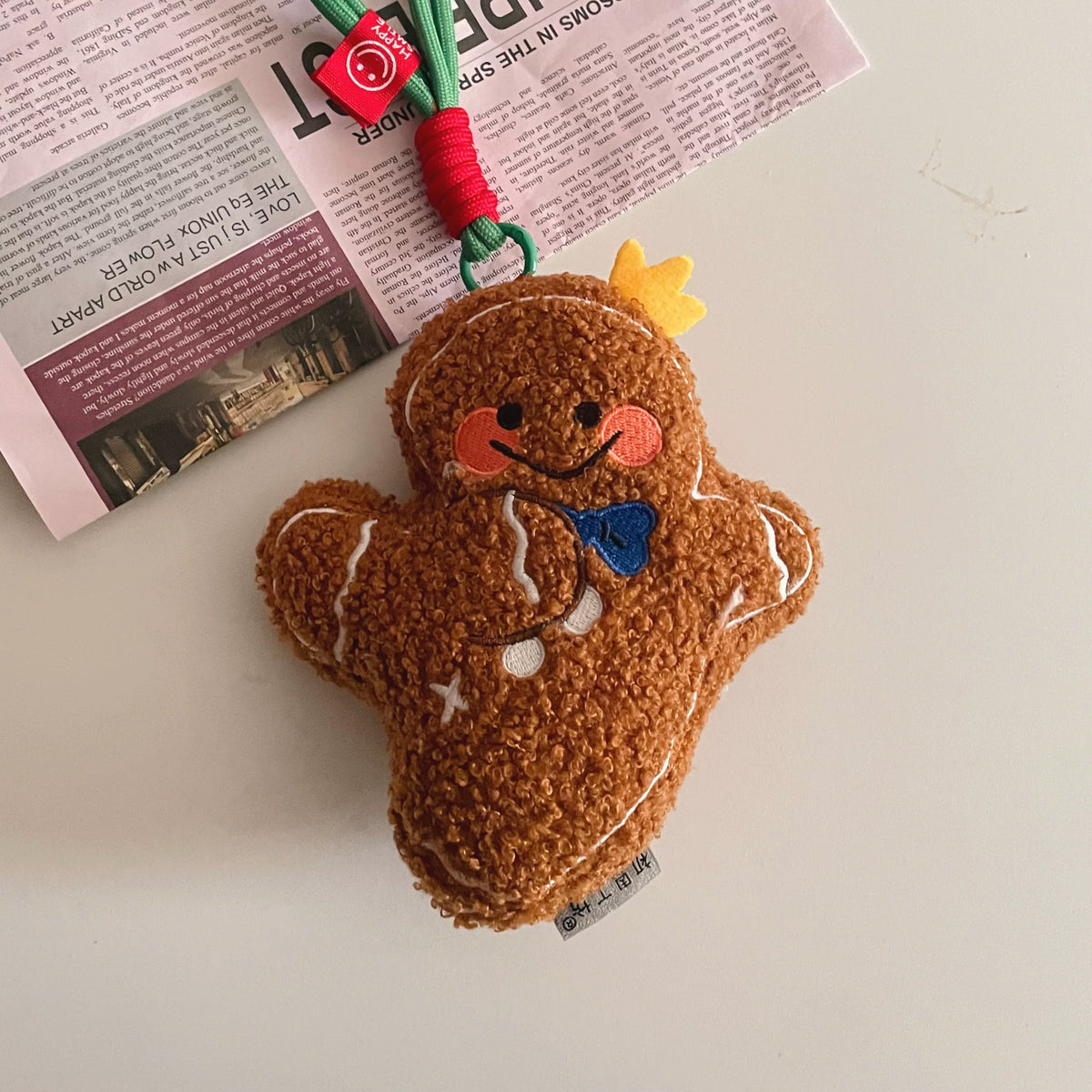 Gingerbread man plush bag charm with yellow crown and hanging cord on a tabletop