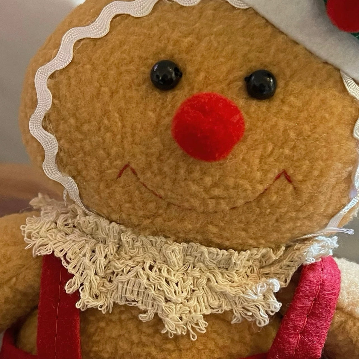 The gingerbread woman doll has black eyes, a round red nose, white icing trim and a cream lace collar.