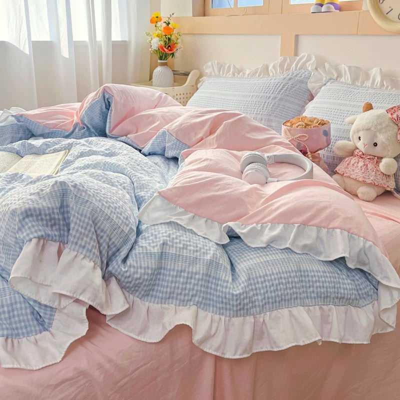 Bed with pink and blue checkered bedding, teddy bear, and snacks in a bright room.