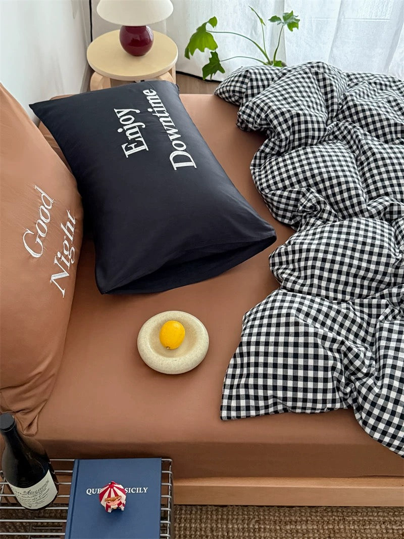 Bed with checkered duvet, 'Enjoy Downtime' pillow, and 'Good Night' pillow.