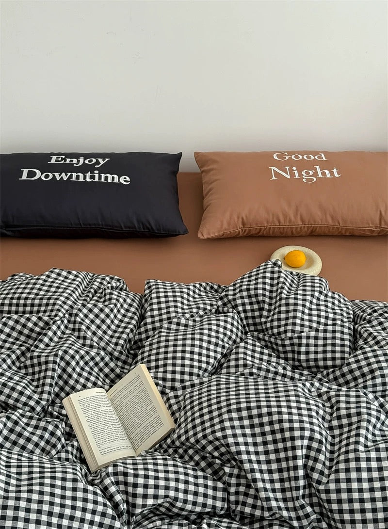 Bed with checkered duvet, open book, and pillows with motivational phrases.