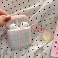 Pink plaid AirPod case with white AirPods on a polka dot fabric background