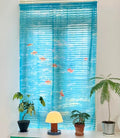 Decorative window blind with fish design on a white wall with plants and a lamp below.