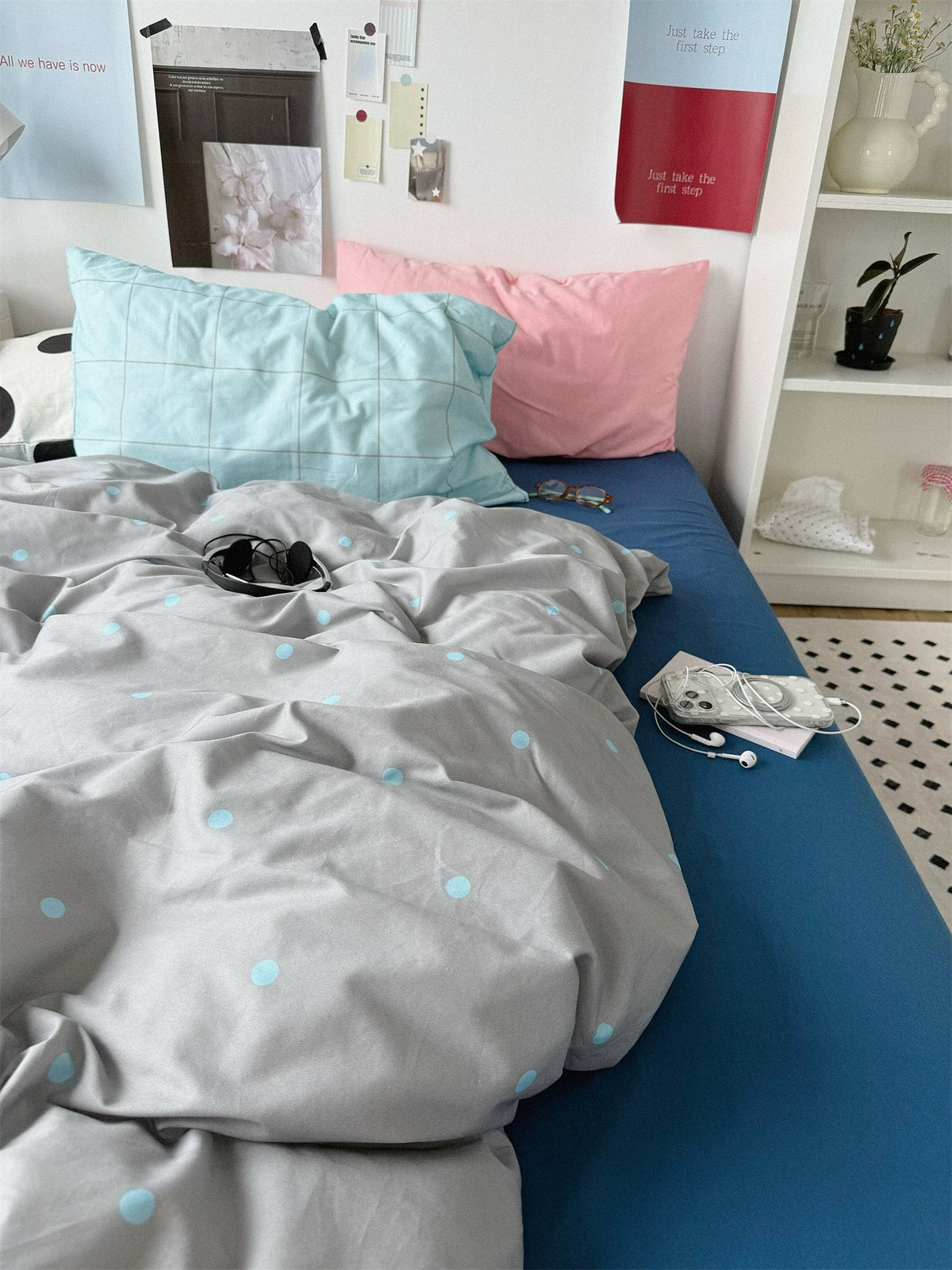 Gray dotted bedding with a blue sheet and pink and blue check pillows viewed from the foot.