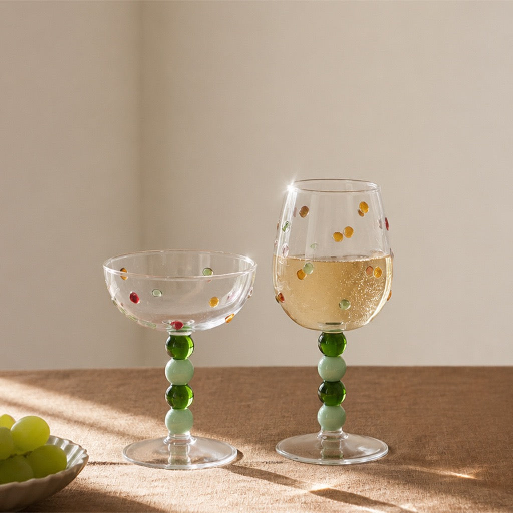 Green ball stem wine glasses with colorful raised dots on a sunlit table